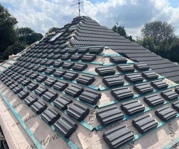 This is a photo of a new hip roof being installed. New felt, battens, and grey tiles have been installed, also a new velux window. Works carried out by WCT Roofing Long Buckby