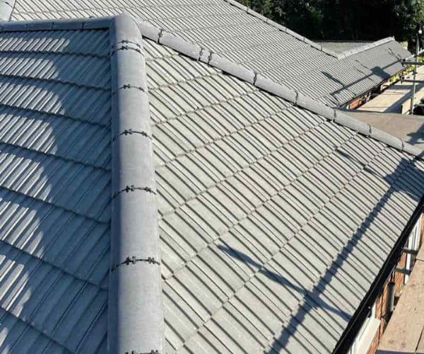 This is a photo of a completed new hip roof installed by WCT Roofing Long Buckby. The photo shows a side elevation, and grey tiles have been used.